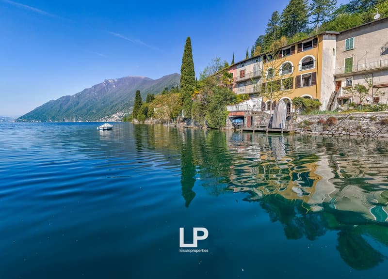 House on the lake, yellow and white building, mountains in the background, trees, dock, boat