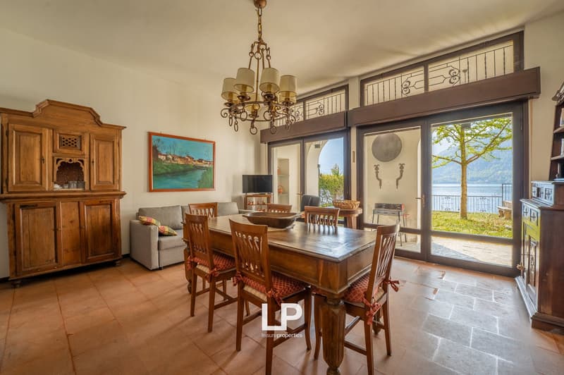 dining room with wooden table, chairs, chandelier, wooden cabinet, couch, TV, painting, sliding glass doors, balcony, lake view
