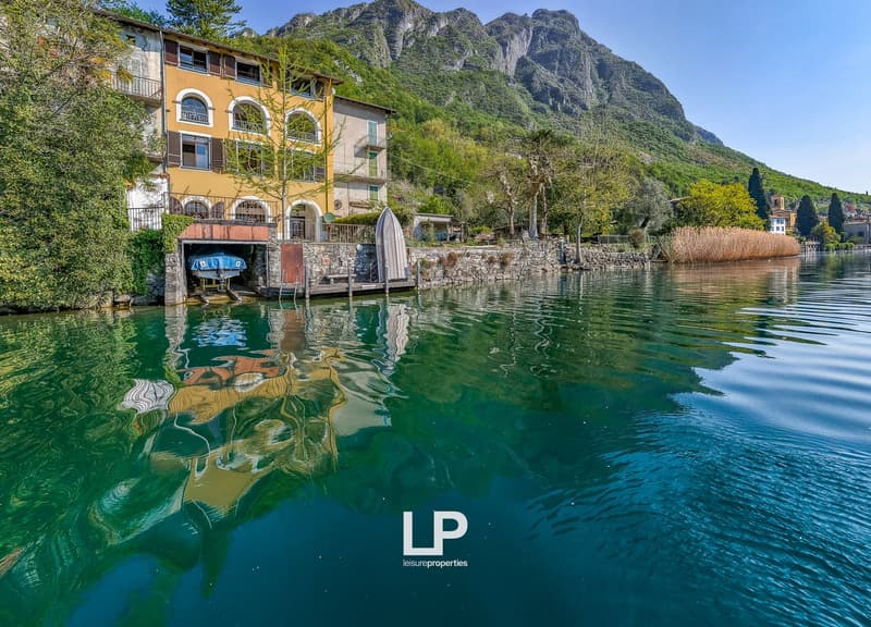 House on the lake, yellow and white facade, mountains in the background, boat dock
