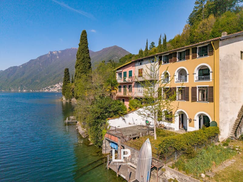 Lakefront house, multiple floors, balconies, surrounded by greenery, mountains in the background