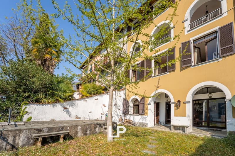 yellow and white building, arched windows, balconies, tree in front, stone bench, stone wall
