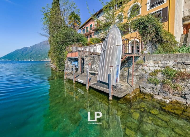 House with a dock on the lake, surrounded by trees and mountains, yellow walls, balcony with railings