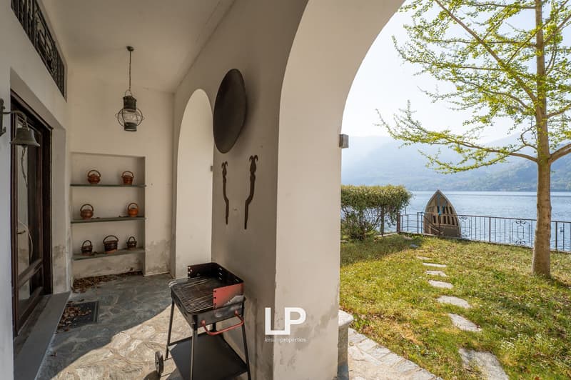 Outdoor area with a barbecue, shelves with teapots, a lake view, and a boat docked on the lake.