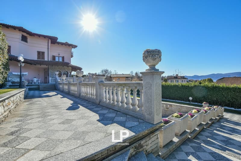 Large villa with a stone walkway, stone balustrade, and a garden with a hedge and flowers