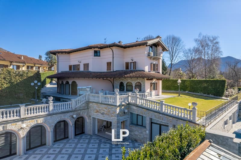 Large villa with multiple floors, balcony, paved driveway, garden with lawn, large windows