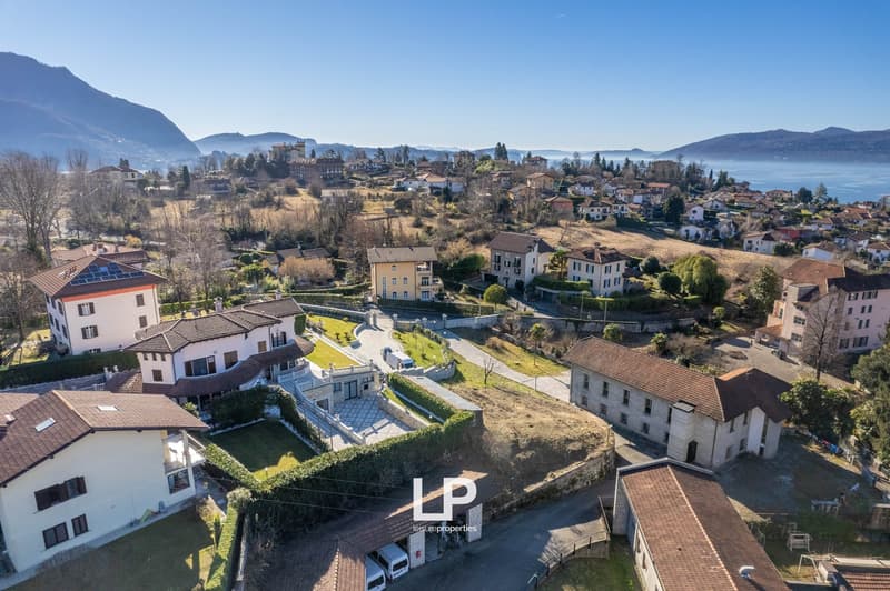 multiple buildings, one appears to be a mansion, located on hillside, mountains and lake in the background