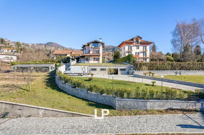 Large villa with multiple floors, surrounded by greenery, driveway, and a white van parked in front.