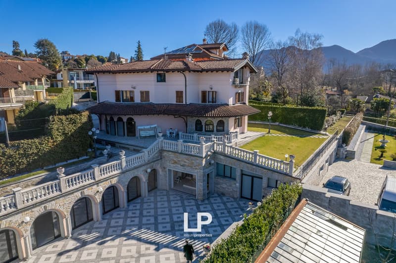 Villa with landscaped garden, tiled terrace, balcony, solar panels, multiple garages, parking areas, and distant mountain views.