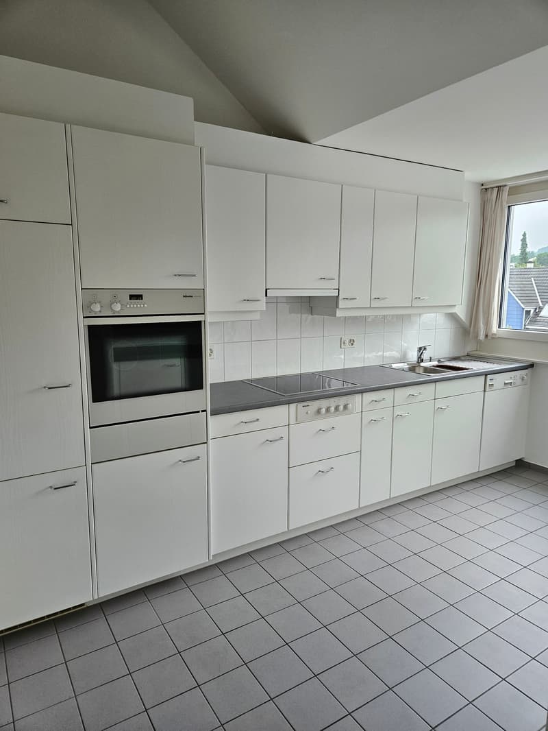 Spacious kitchen with white cabinets, built-in oven, and tile flooring. The kitchen appears to have a dishwasher and a modern, minimalist design.