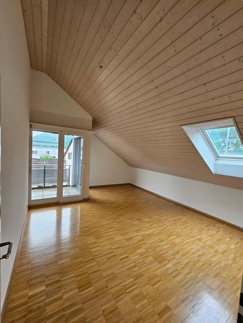Spacious empty attic room, sliding glass doors to balcony, wooden floor, sloped ceiling, window at end