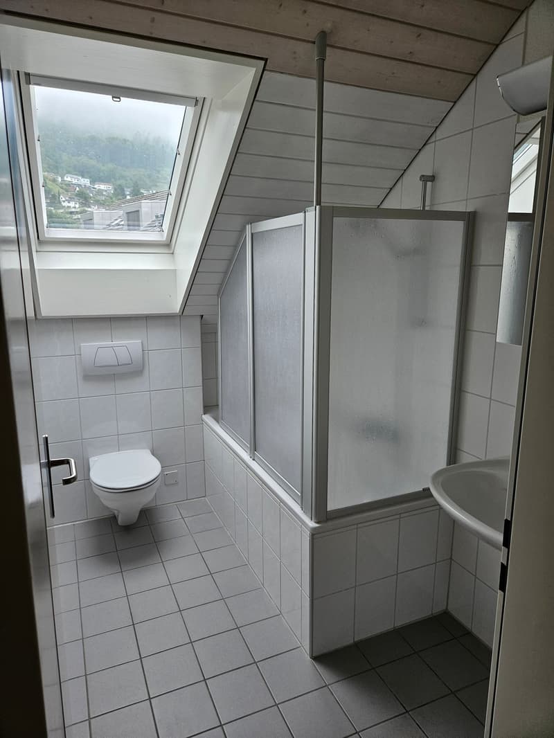 Bathroom with tiled floor, toilet, shower enclosure, and a window with a view of the outdoors.