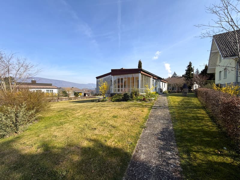 Detached house, large glass windows, surrounded by a garden, gravel path, mountains in the background
