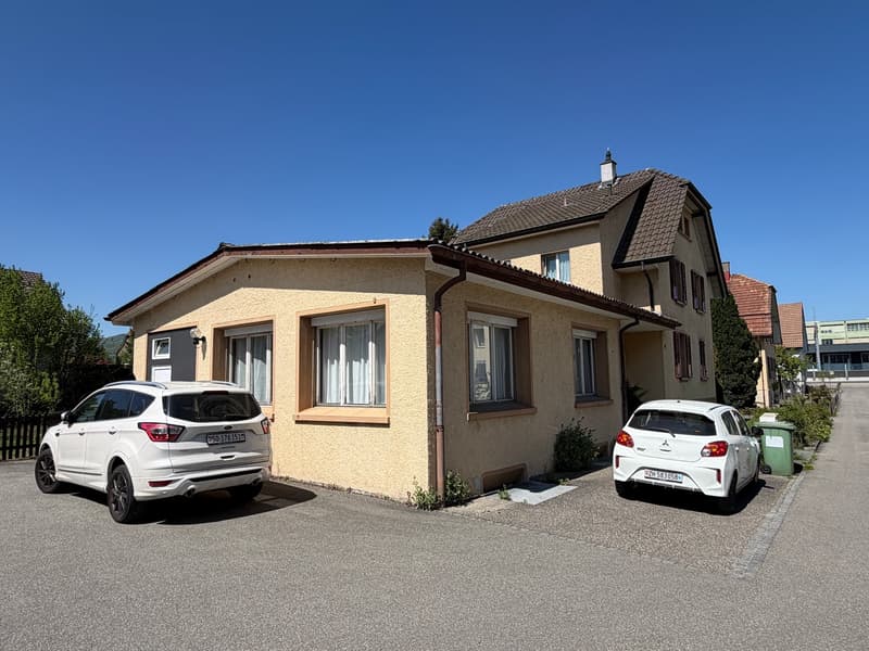 Single family house, beige exterior, 2 cars parked in front, 2 windows, chimney, small garden