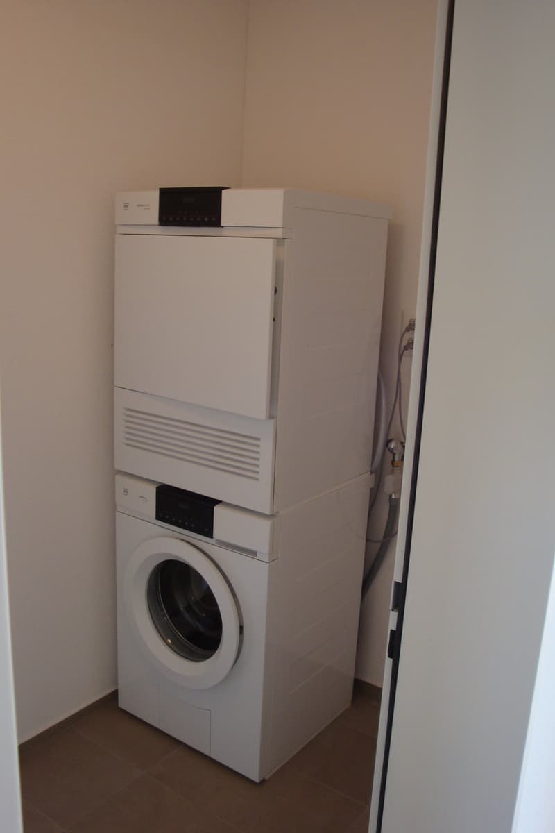 A white washing machine and dryer stacked on top of each other in a corner of a room.