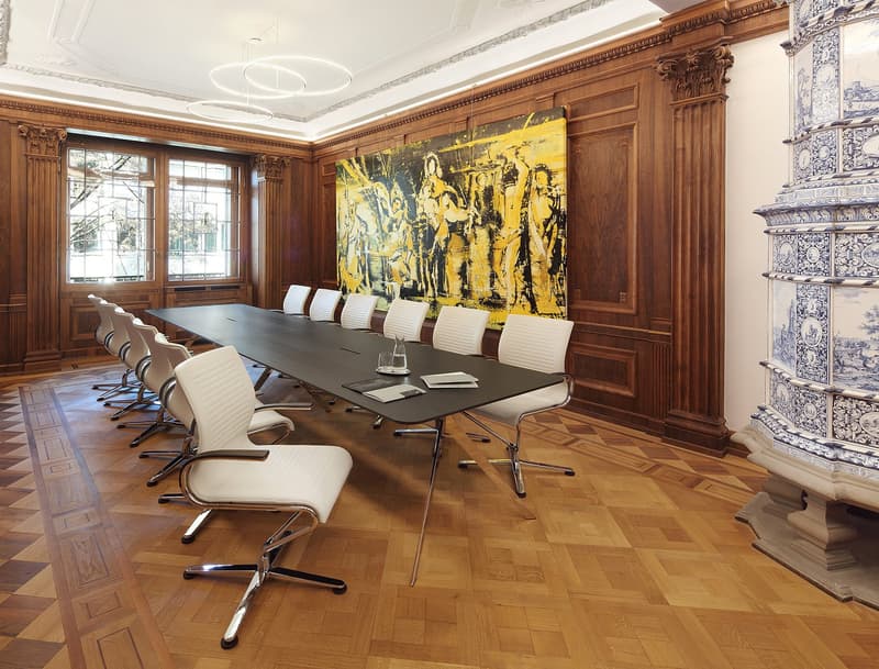 Large conference table, white leather chairs, wooden paneled walls, large artwork, glass windows, parquet floor
