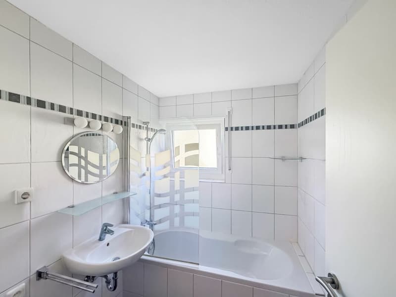 BAdezimmer mit Badewanne und integrierter Dusche sowie Lavabo und Fenster.