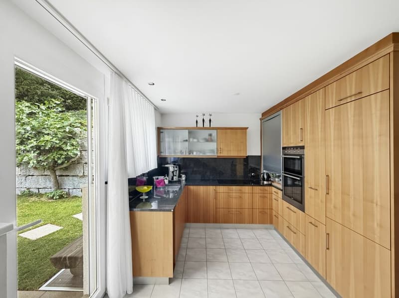 Die helle Küche mit Sitzbank, hochwertigen Fronten und Einbaugeräten sowie direktem Zugang zur Terrasse