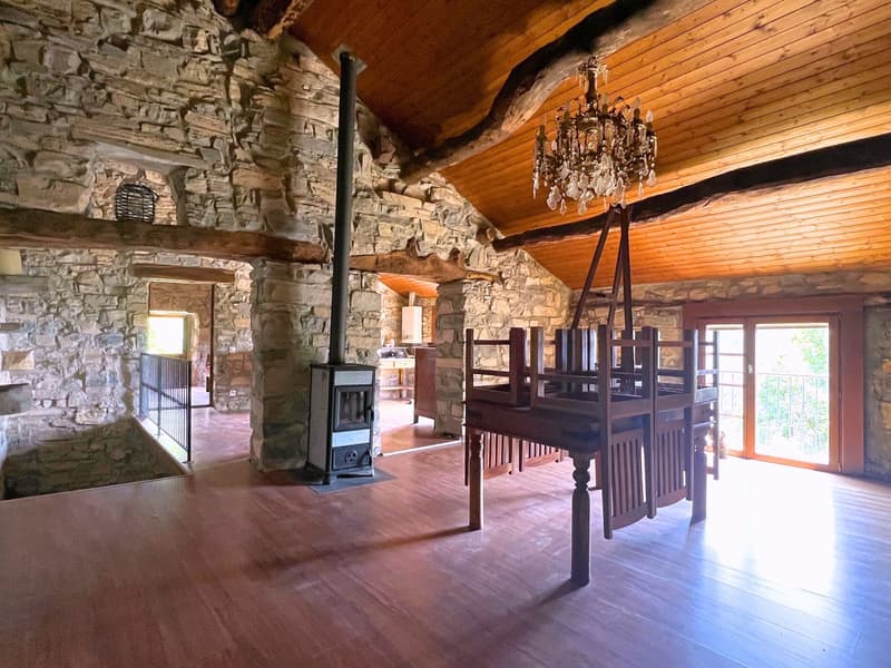Large room with exposed stone walls, wooden floor, chandelier, fireplace, staircase, balcony, sliding glass doors, balcony