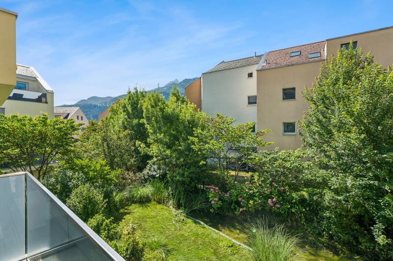 A balcony view of a small garden with green lawn, trees, bushes and flowers.