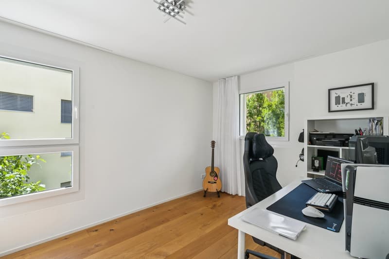 Empty room, two large windows, hardwood floor, black office chair, desk with laptop, computer tower, guitar, white walls, small table, picture frame