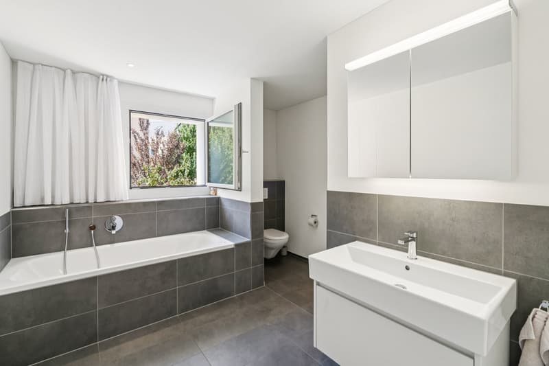 White sink, bathtub with shower, toilet, mirror, gray tiles, white curtains