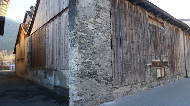 Old building with wooden wall and stone wall, large wooden doors, small windows, located on a street