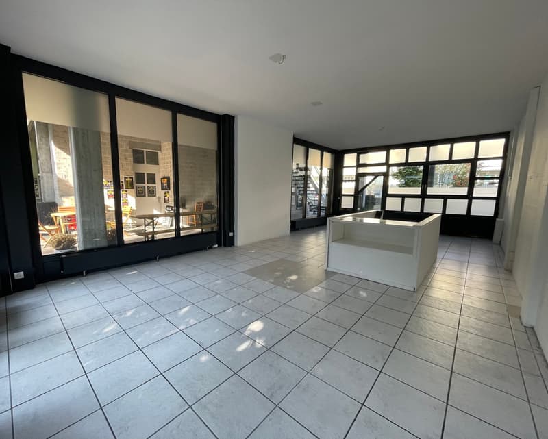Empty room with white tiles, large windows, white reception desk, and a view of the outside