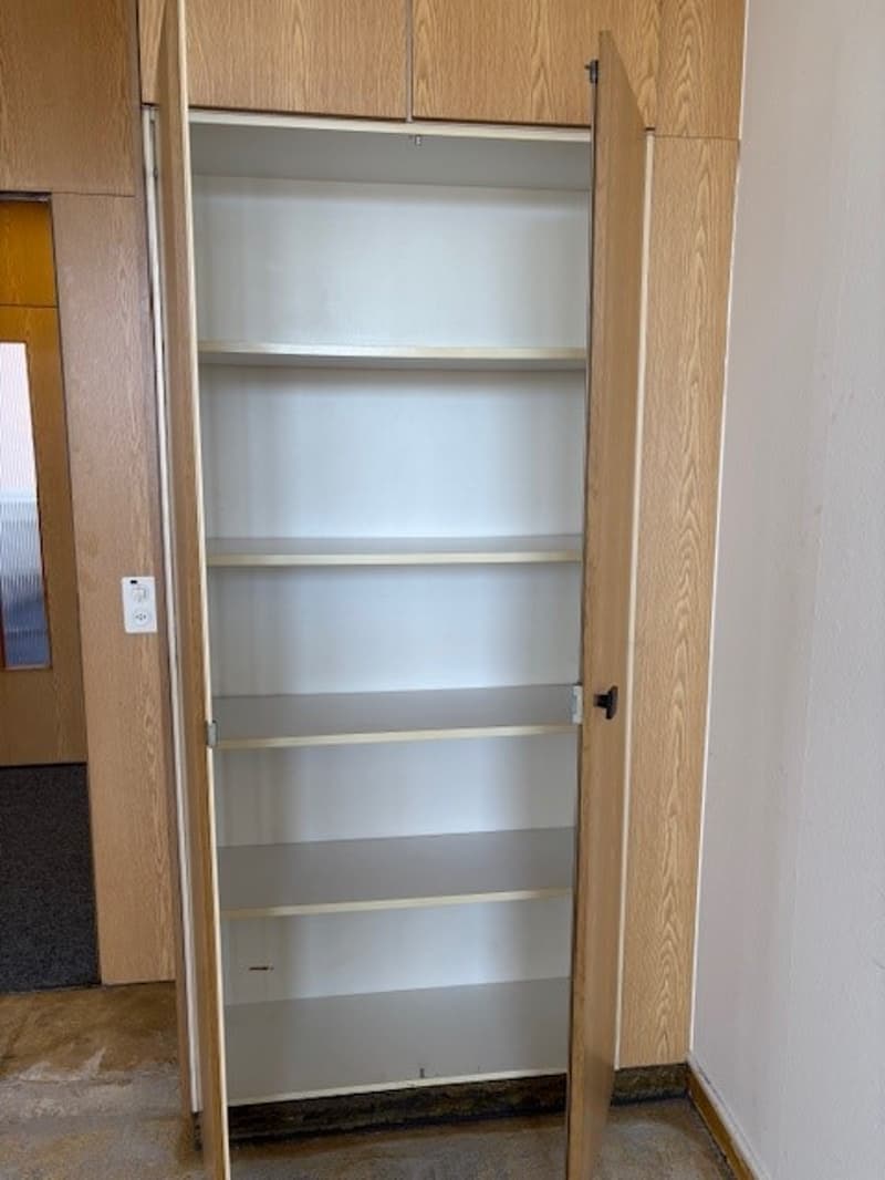 The image shows a built-in storage closet with multiple shelves. The closet has a wooden exterior and the interior shelves are white in color.