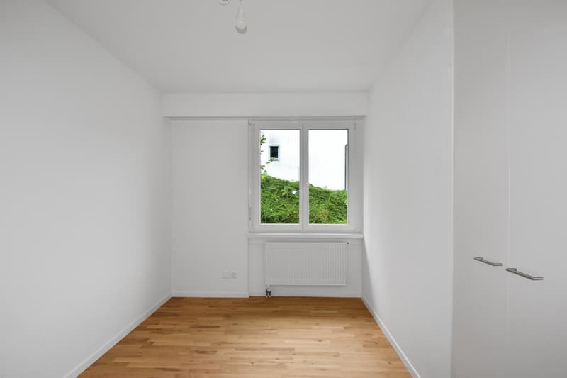 modern design, white walls, wooden floor, double window with white frames, white radiator below the window, door on the right side