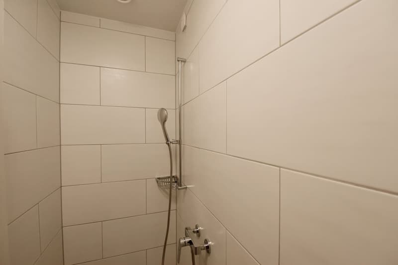 white tiled walls, stainless steel shower head, shower rod, small basket