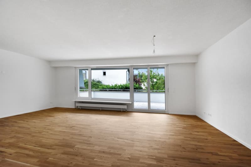 Empty room with wooden floors, white walls, sliding glass doors to a balcony