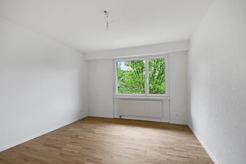 empty room with white walls, wooden floor, large window, white radiator