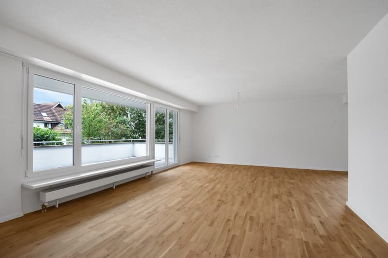 Empty room, hardwood floors, large windows, white walls, balcony, sliding glass doors, radiator.