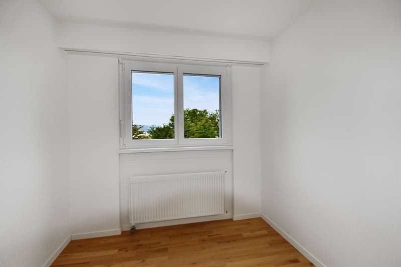 Empty room with white walls, wooden floor, white window, radiator