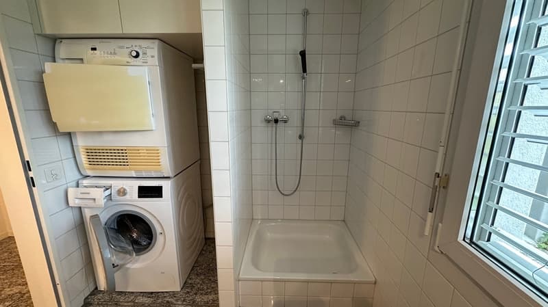 Bathroom with a washing machine, dishwasher, and a shower stall with tiled walls