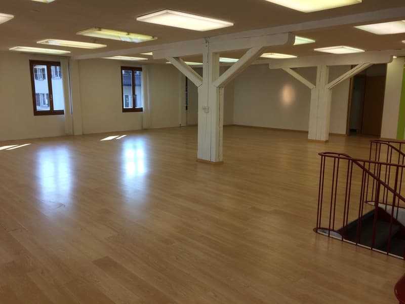 empty room, wooden floor, white ceiling with lights, two windows on the left, red staircase on the right