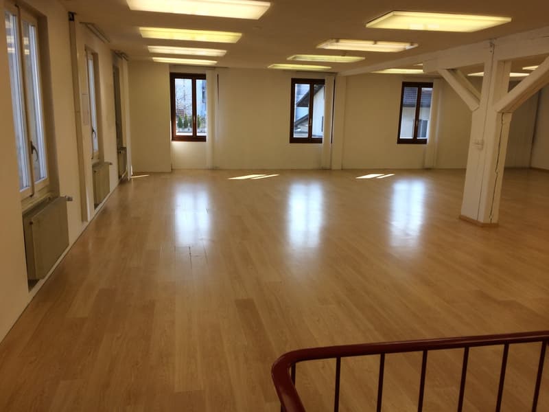 Open room with hardwood floors, windows, and radiators, high ceiling, fluorescent lights