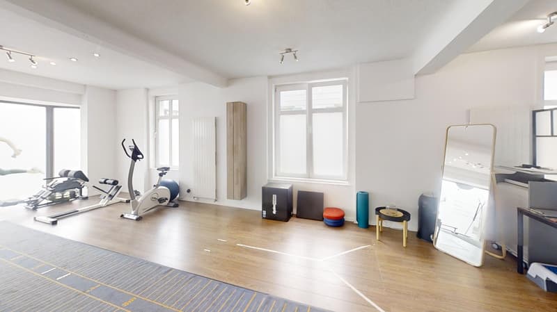 Spacious room with hardwood floors, large windows, exercise equipment including a treadmill and weight training machines, storage cabinets, and various fitness accessories