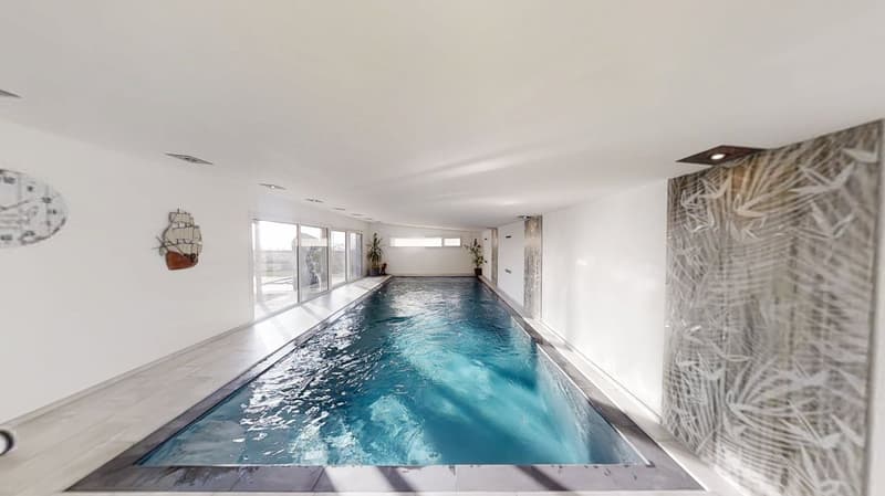An indoor pool with white walls, tiles on the floor, and glass windows