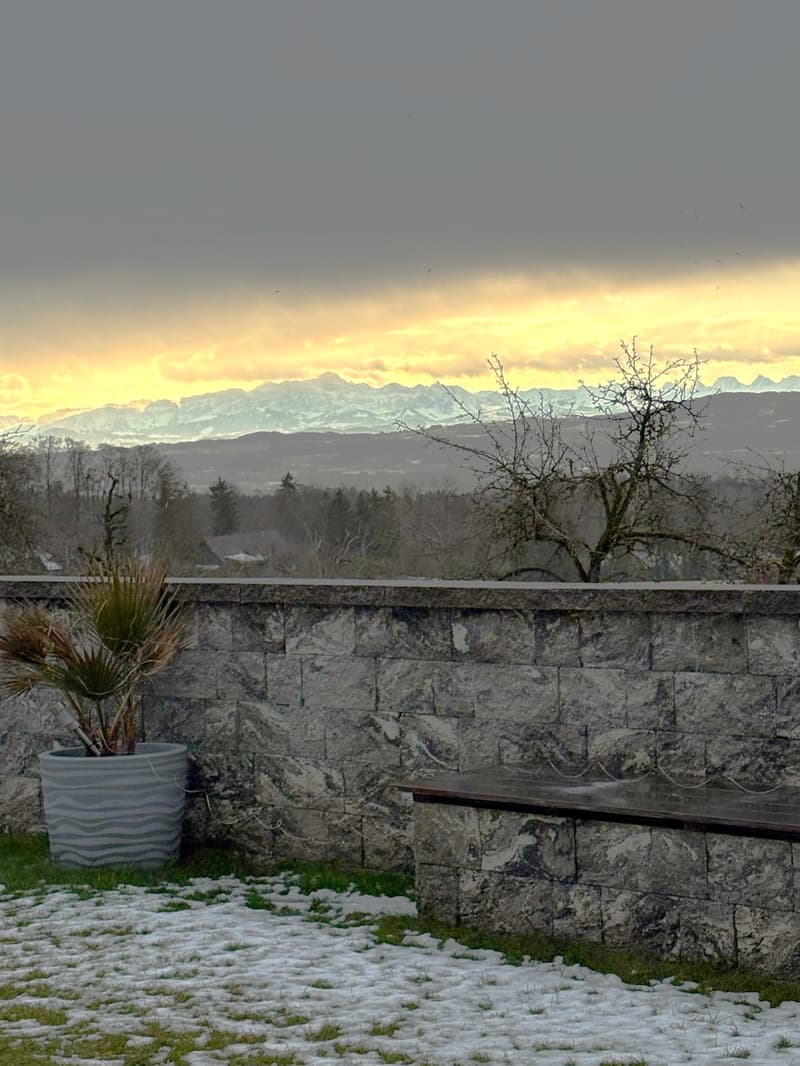snow covered grassy area with stone bench and planter, view of mountains