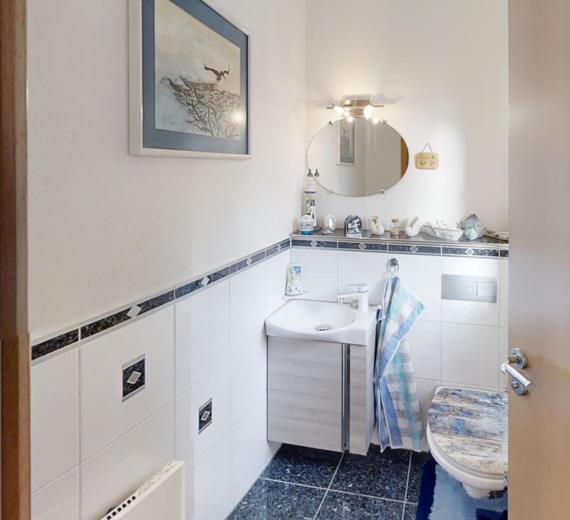 White bathroom with a sink, toilet, wall-mounted mirror, and towel rack.