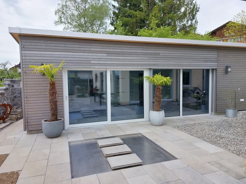 Single story building, glass sliding doors, gray exterior, gravel path, central drainage