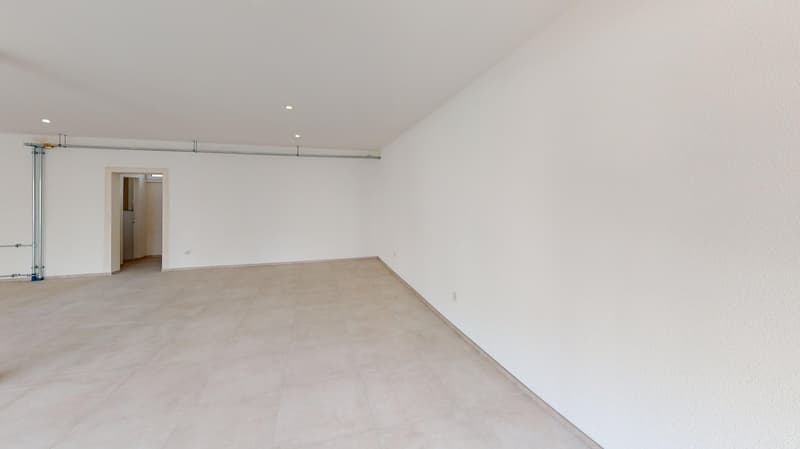 Empty room with white tiles, white walls, ceiling lights, doorway to another room.