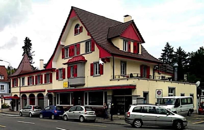 yellow building, red accents, several windows, arched window, balcony, red roof, cars parked on street