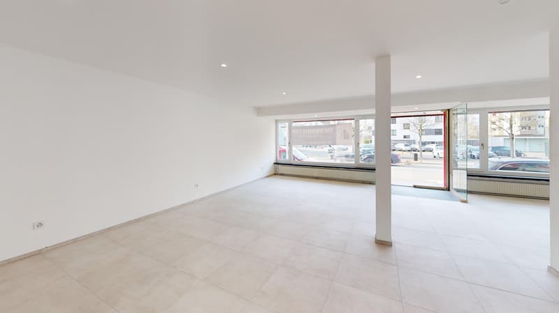 Empty room with white walls, tile floor, large windows, and a door leading to an open area