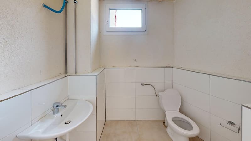 a small bathroom with sink, toilet, window, pipes