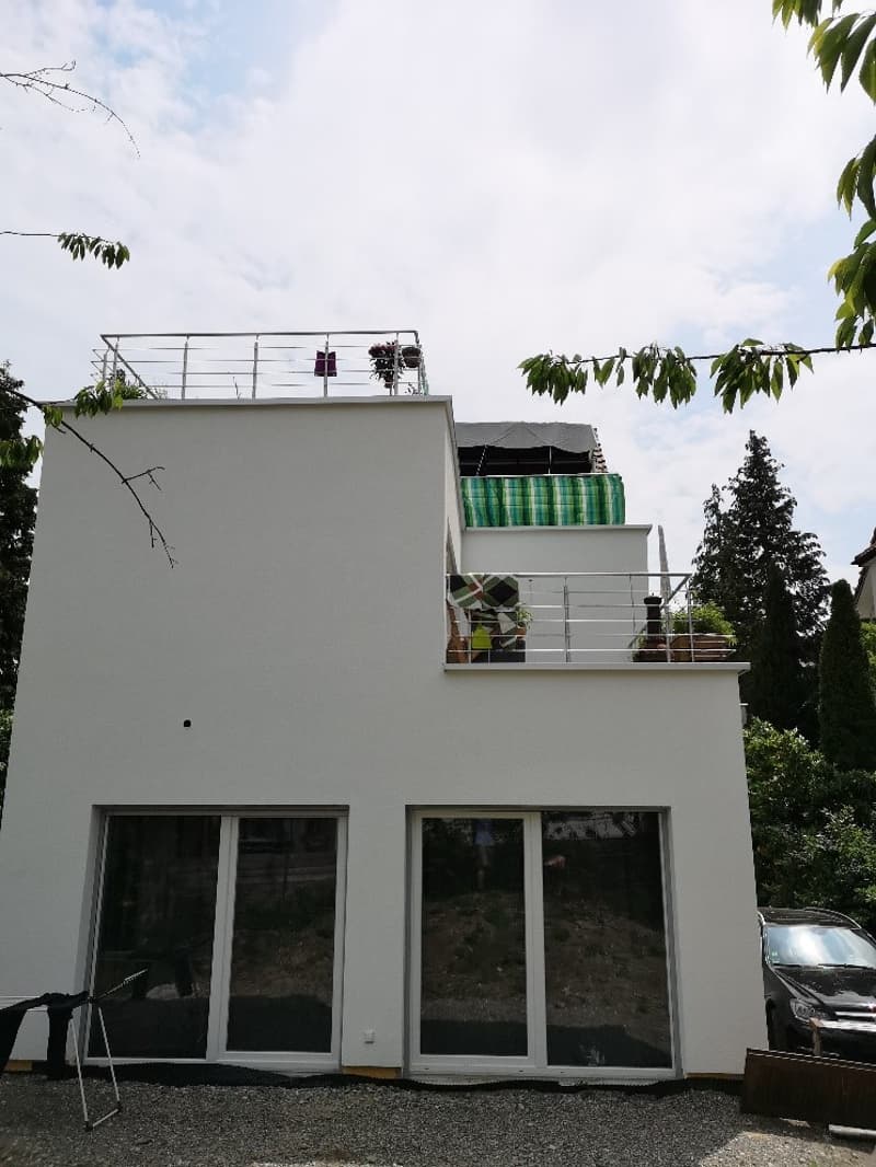modern white house, 3 floors, large glass windows, balcony on the second floor, metal railings, plants on the balcony, gravel driveway