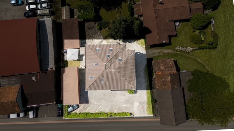 Aerial view of residential properties, main house with two smaller annexes, asphalt driveway and multiple parking spaces for vehicles.