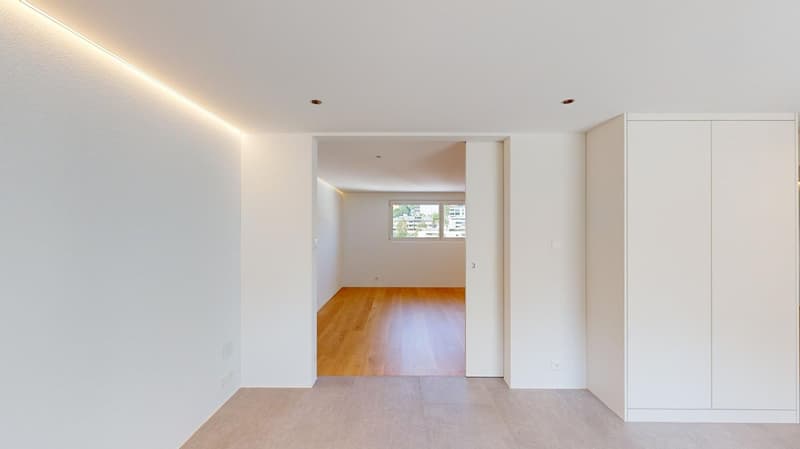 Empty room with white walls, wooden floor, and a window with a view