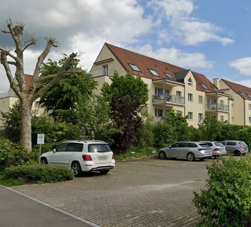 Apartment building with red roof, balconies, multiple cars parked in front